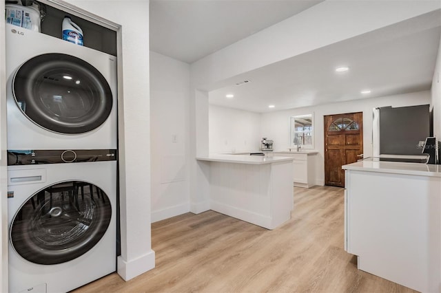 laundry area with light wood-style floors, laundry area, baseboards, and stacked washer and clothes dryer