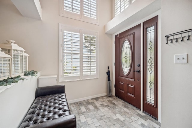 foyer featuring a healthy amount of sunlight, brick floor, a towering ceiling, and baseboards