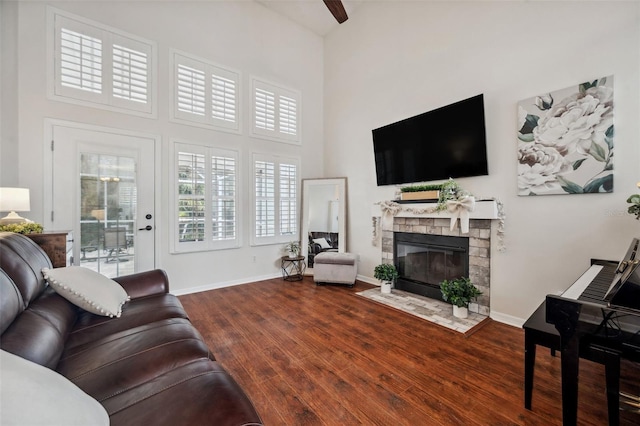 living room featuring a stone fireplace, wood finished floors, a high ceiling, and baseboards