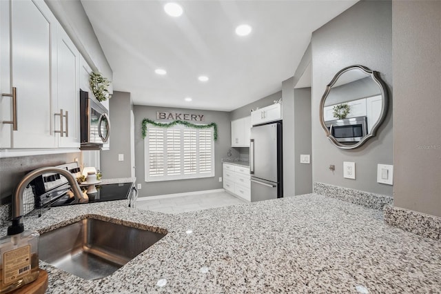 kitchen featuring stainless steel appliances, recessed lighting, white cabinetry, a sink, and light stone countertops