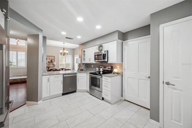 kitchen featuring appliances with stainless steel finishes, white cabinetry, visible vents, and light stone countertops