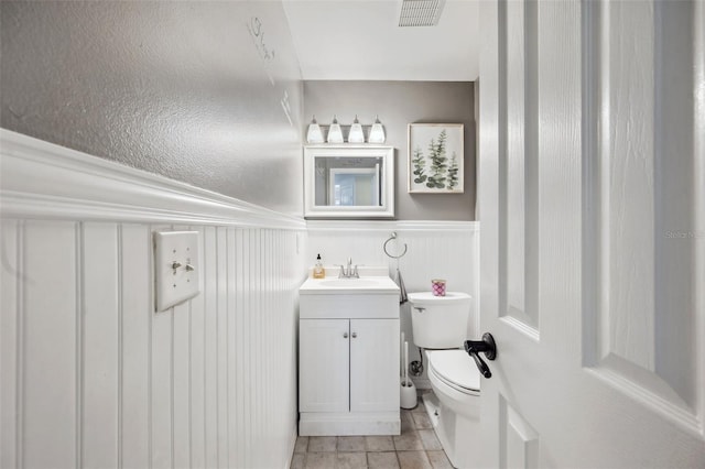 half bathroom with a wainscoted wall, visible vents, vanity, and toilet