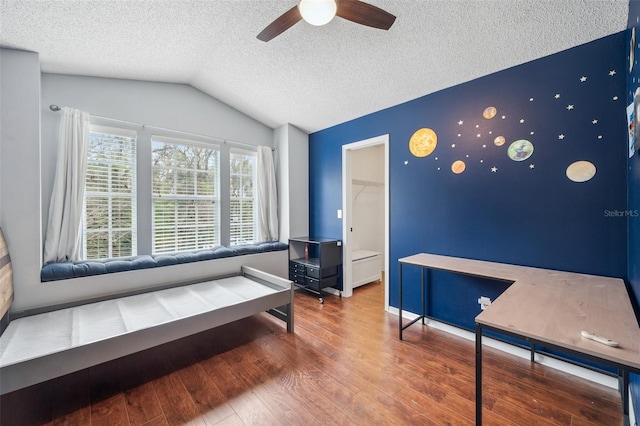 bedroom featuring lofted ceiling, a textured ceiling, an accent wall, wood finished floors, and a spacious closet