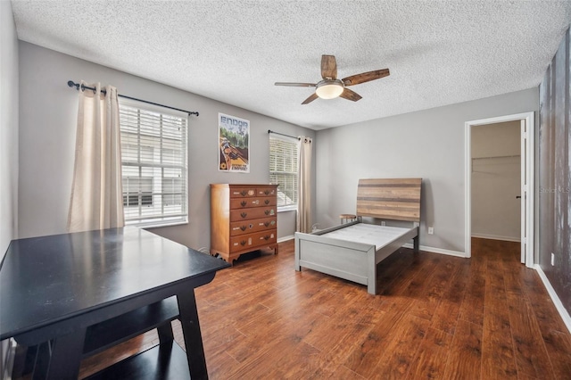 bedroom featuring a textured ceiling, a ceiling fan, baseboards, a spacious closet, and dark wood finished floors