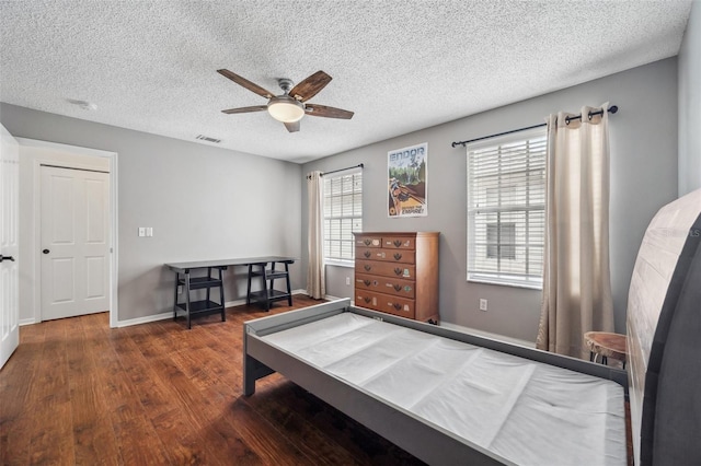 bedroom with baseboards, visible vents, ceiling fan, dark wood-type flooring, and a textured ceiling