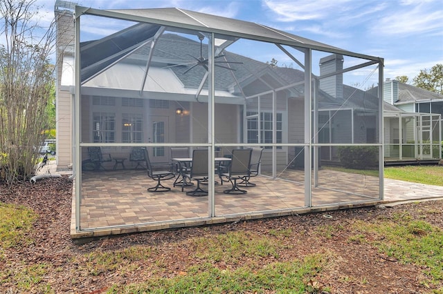 back of property featuring glass enclosure, a chimney, and a patio area