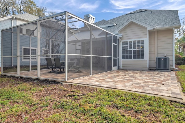 back of house with a shingled roof, a patio, a chimney, a lanai, and cooling unit