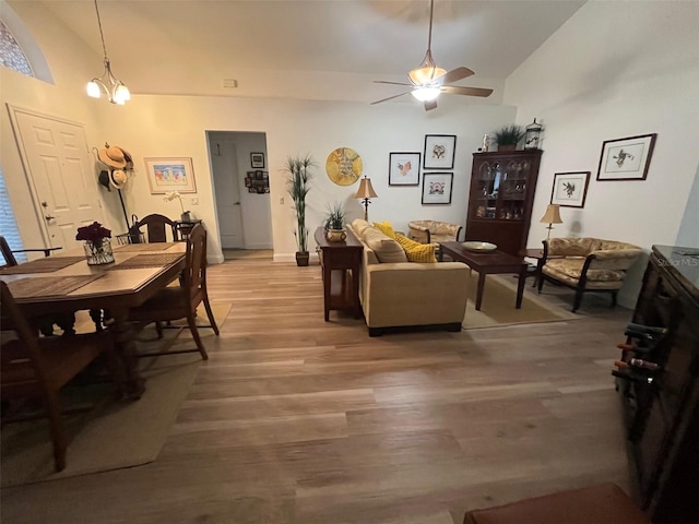 living room featuring high vaulted ceiling, light wood finished floors, and ceiling fan with notable chandelier