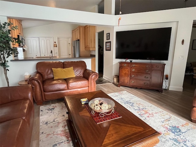 living area featuring vaulted ceiling, light wood-style flooring, and baseboards