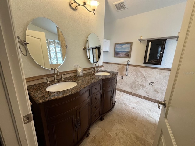 bathroom with double vanity, tile walls, visible vents, and a sink