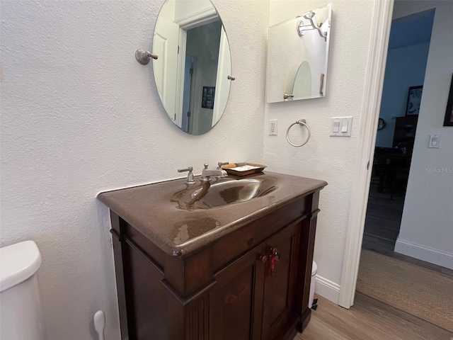 half bathroom featuring baseboards, vanity, toilet, and wood finished floors