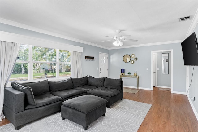 living area featuring wood finished floors, baseboards, visible vents, ornamental molding, and ceiling fan