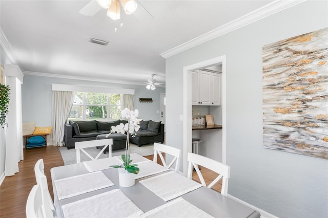 dining space featuring visible vents, wood finished floors, a ceiling fan, and crown molding