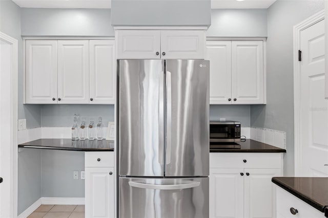 kitchen with dark countertops, light tile patterned floors, appliances with stainless steel finishes, and white cabinetry