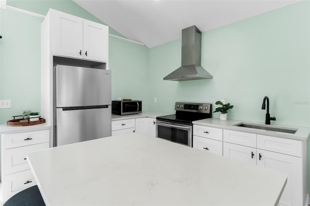 kitchen featuring a sink, stainless steel appliances, vaulted ceiling, white cabinetry, and wall chimney range hood