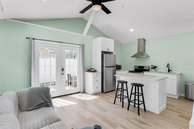 kitchen featuring a kitchen breakfast bar, white cabinetry, french doors, appliances with stainless steel finishes, and wall chimney range hood