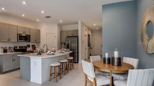 kitchen featuring a center island with sink, gray cabinets, light countertops, visible vents, and appliances with stainless steel finishes