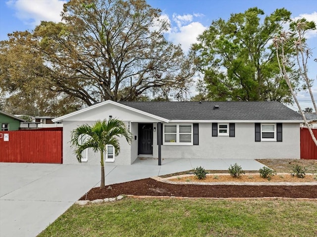 ranch-style home featuring driveway, roof with shingles, fence, and stucco siding