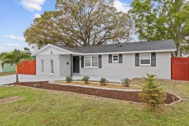 ranch-style home with a front yard, roof with shingles, fence, and stucco siding