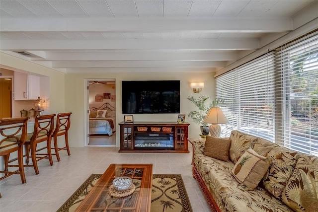 living room featuring a healthy amount of sunlight, visible vents, beam ceiling, and a glass covered fireplace