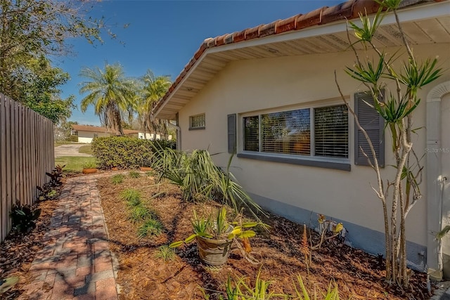 view of home's exterior with a tiled roof, fence, and stucco siding