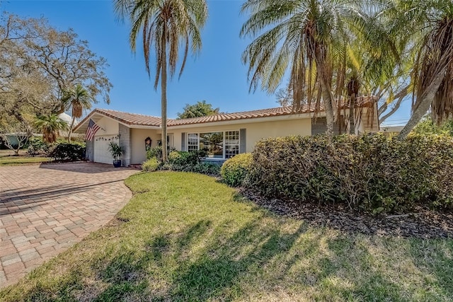 single story home featuring a front yard, an attached garage, a tile roof, and stucco siding