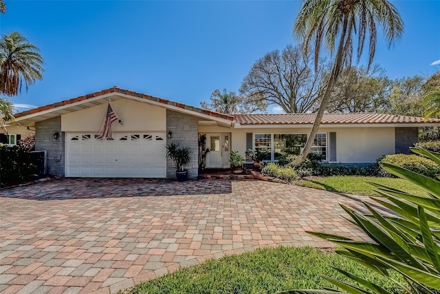 ranch-style home featuring a garage, decorative driveway, a tile roof, and stucco siding