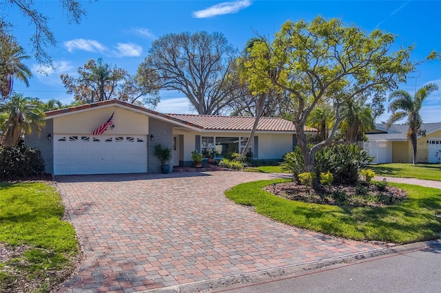 ranch-style house with an attached garage, a tiled roof, decorative driveway, stucco siding, and a front lawn