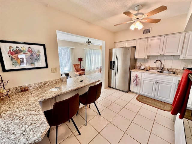 kitchen featuring visible vents, white cabinets, stainless steel fridge with ice dispenser, light stone counters, and a sink