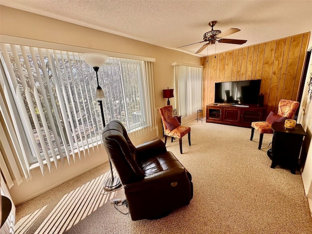 sitting room with wood walls, ceiling fan, a textured ceiling, and carpet flooring