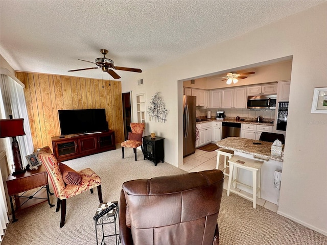 living room featuring light colored carpet, visible vents, ceiling fan, wooden walls, and a textured ceiling