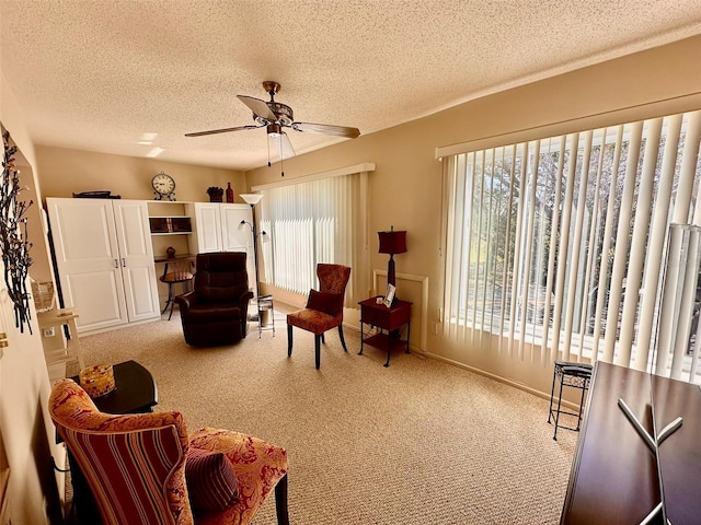 sitting room featuring a textured ceiling, baseboards, a ceiling fan, and light colored carpet