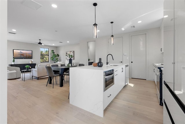 kitchen with a kitchen island with sink, stainless steel oven, white cabinetry, light countertops, and pendant lighting