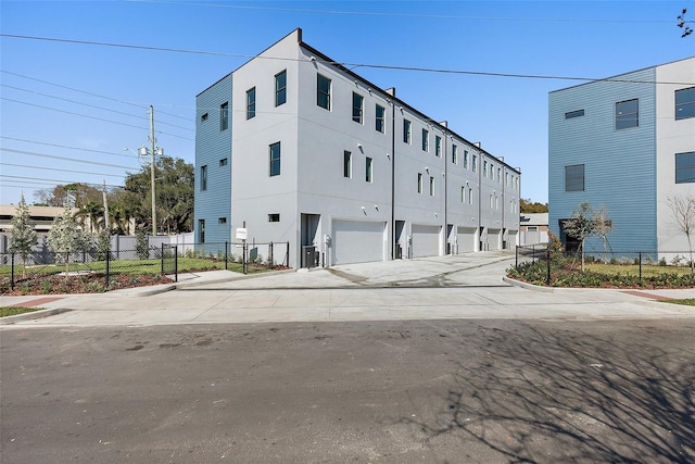 view of building exterior featuring concrete driveway, an attached garage, and fence