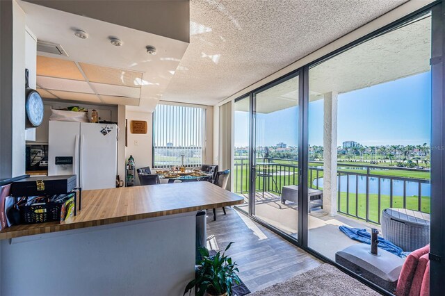 kitchen with butcher block counters, a water view, wood finished floors, floor to ceiling windows, and white fridge with ice dispenser