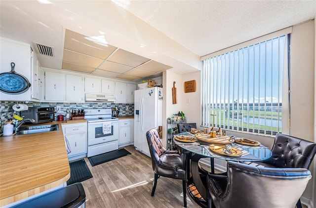 kitchen featuring white appliances, visible vents, range hood, decorative backsplash, and light wood finished floors