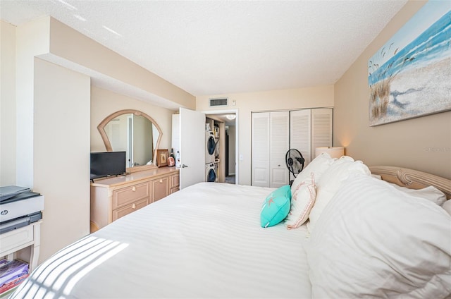 bedroom featuring a textured ceiling, a closet, visible vents, and stacked washer / drying machine