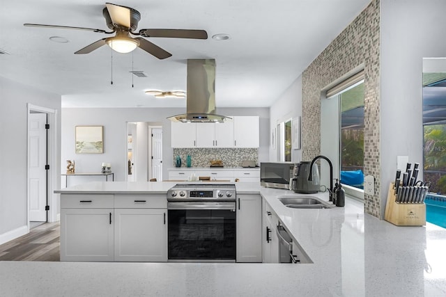 kitchen with island range hood, light stone countertops, stainless steel appliances, white cabinetry, and a sink