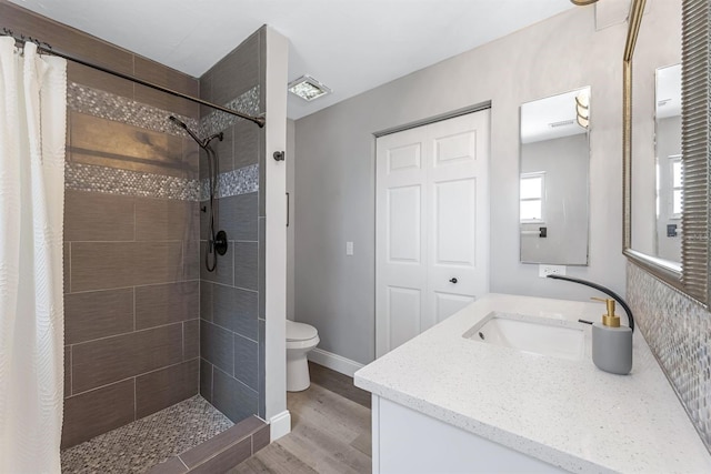 bathroom featuring vanity, wood finished floors, a tile shower, and toilet