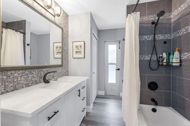 bathroom featuring baseboards, wood finished floors, shower / bath combination with curtain, vanity, and backsplash