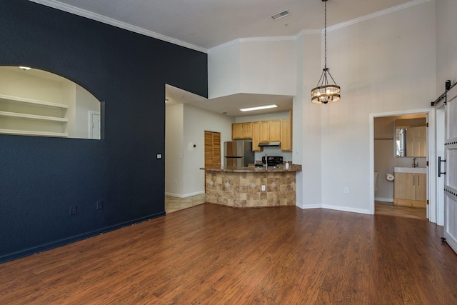 unfurnished living room with a barn door, built in features, visible vents, ornamental molding, and wood finished floors