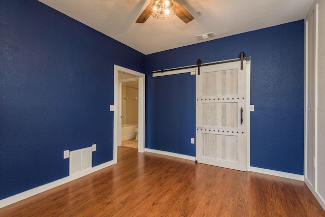 unfurnished bedroom featuring a barn door, wood finished floors, and visible vents