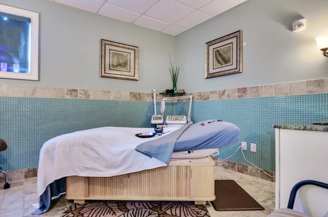 tiled bedroom featuring wainscoting, a drop ceiling, and tile walls