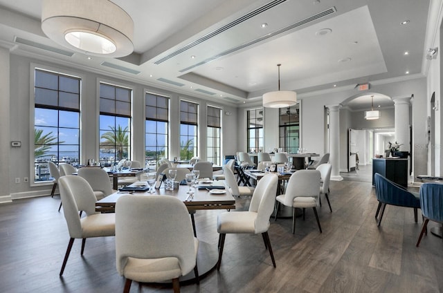 dining area with dark wood-style flooring, a raised ceiling, decorative columns, and crown molding