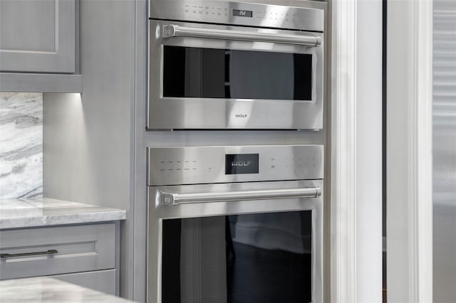 details featuring light stone counters, stainless steel double oven, and gray cabinetry