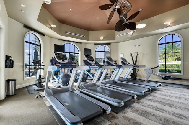 gym with a healthy amount of sunlight, recessed lighting, a raised ceiling, and baseboards