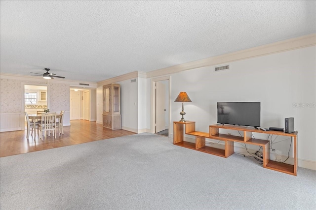 living room featuring visible vents, a ceiling fan, light colored carpet, crown molding, and a textured ceiling