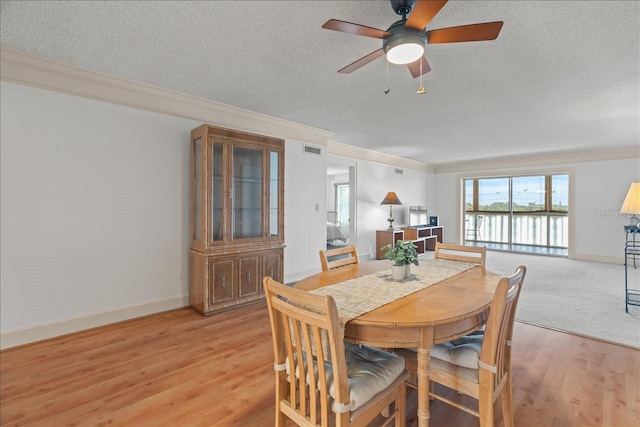 dining space featuring baseboards, visible vents, light wood-style flooring, ornamental molding, and a textured ceiling