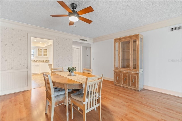 dining space featuring a textured ceiling, wainscoting, visible vents, and wallpapered walls