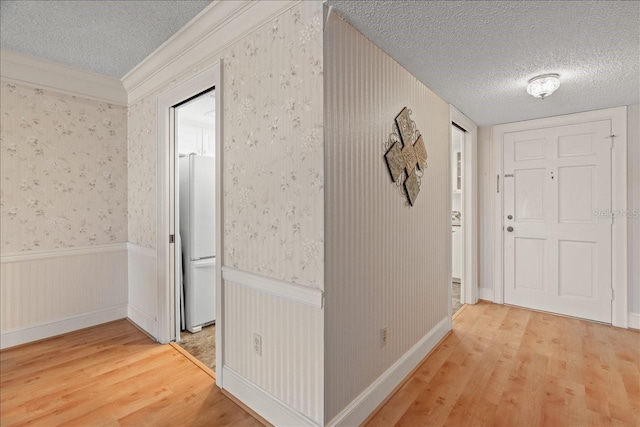 hallway featuring wood finished floors, a textured ceiling, and wallpapered walls